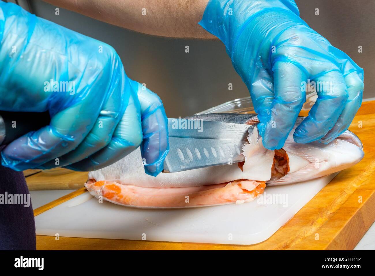 Les mains d'un cuisinier mâle en gants hygiéniques coupent la tête d'un  saumon avec un couteau. Couper du poisson frais dans la cuisine sur une  planche à découper Photo Stock - Alamy