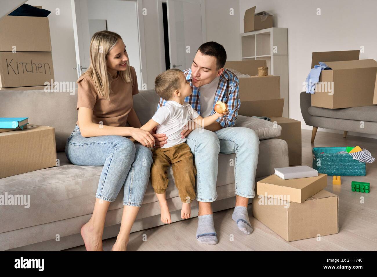 Une famille heureuse avec un enfant assis sur un canapé à la maison lors d'une journée de déménagement. Banque D'Images