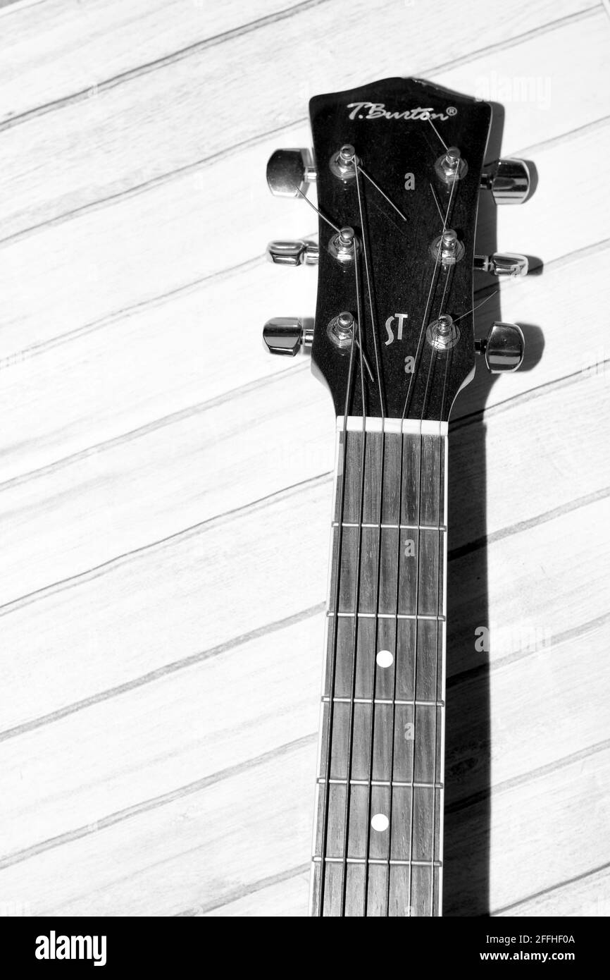 Gros plan noir et blanc de la poupée et du cou d'une guitare acoustique sur un fond de bois de planche texturé et lumineux Banque D'Images
