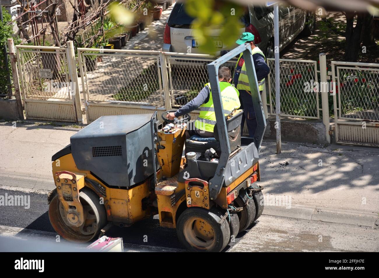 NIS, Serbie - 24 avril 2021: Petit compacteur pneumatique à rouleaux à bandage sur la chaussée asphaltée travaille pour la réparation de routes avec des ouvriers en uniforme vert Banque D'Images