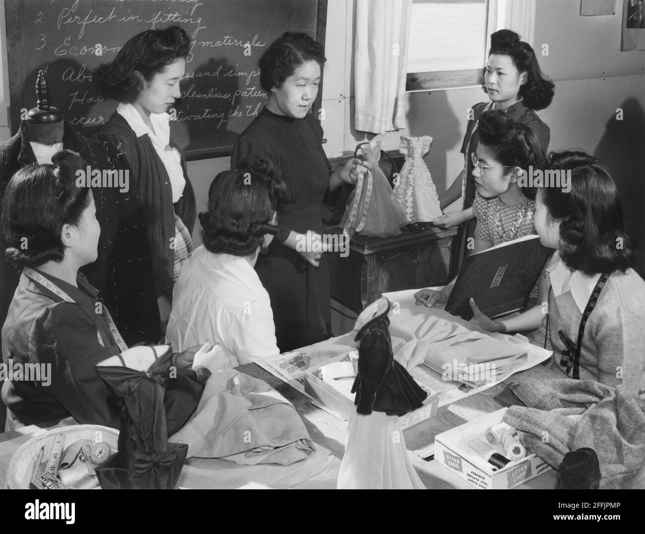 Mme Ryie Yoshizawa, enseignante de mode et de design, avec un groupe d'étudiants à table avec des équipements de tissus et de confection de vêtements, Manzanar Relocation Center, Californie, Etats-Unis, Ansel Adams, Collection Manzanar War Relocation Centre, 1943 Banque D'Images