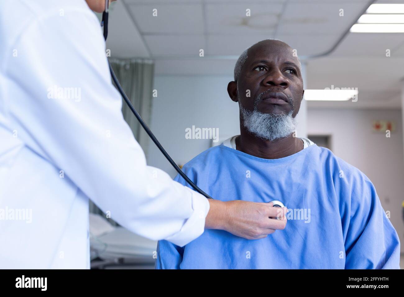 Femme caucasienne médecin examinant avec stéthoscope afro-américain patient mâle dans la chambre d'hôpital Banque D'Images