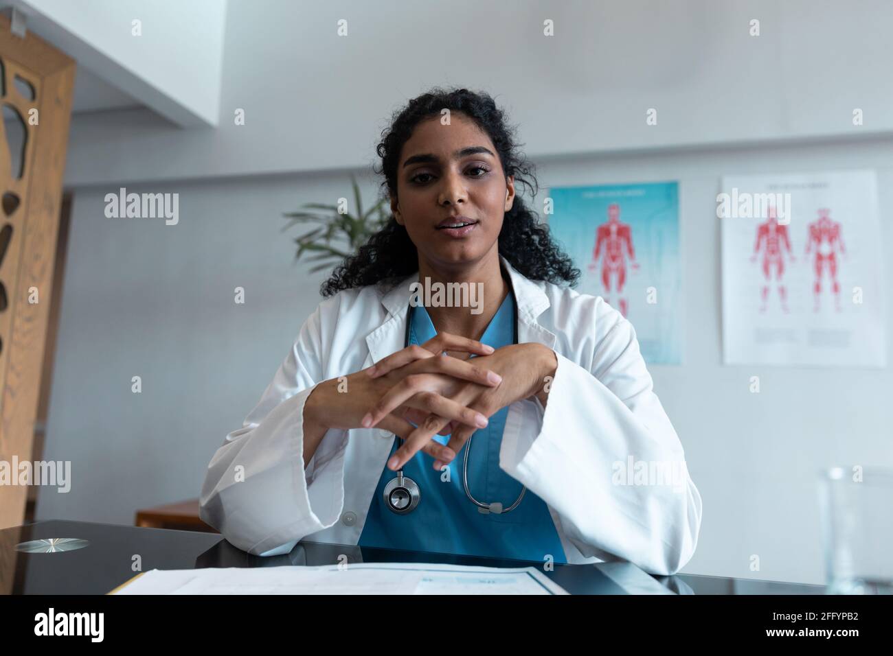 Femme de race mixte médecin à la table de parler et de gesturer pendant consultation par appel vidéo Banque D'Images