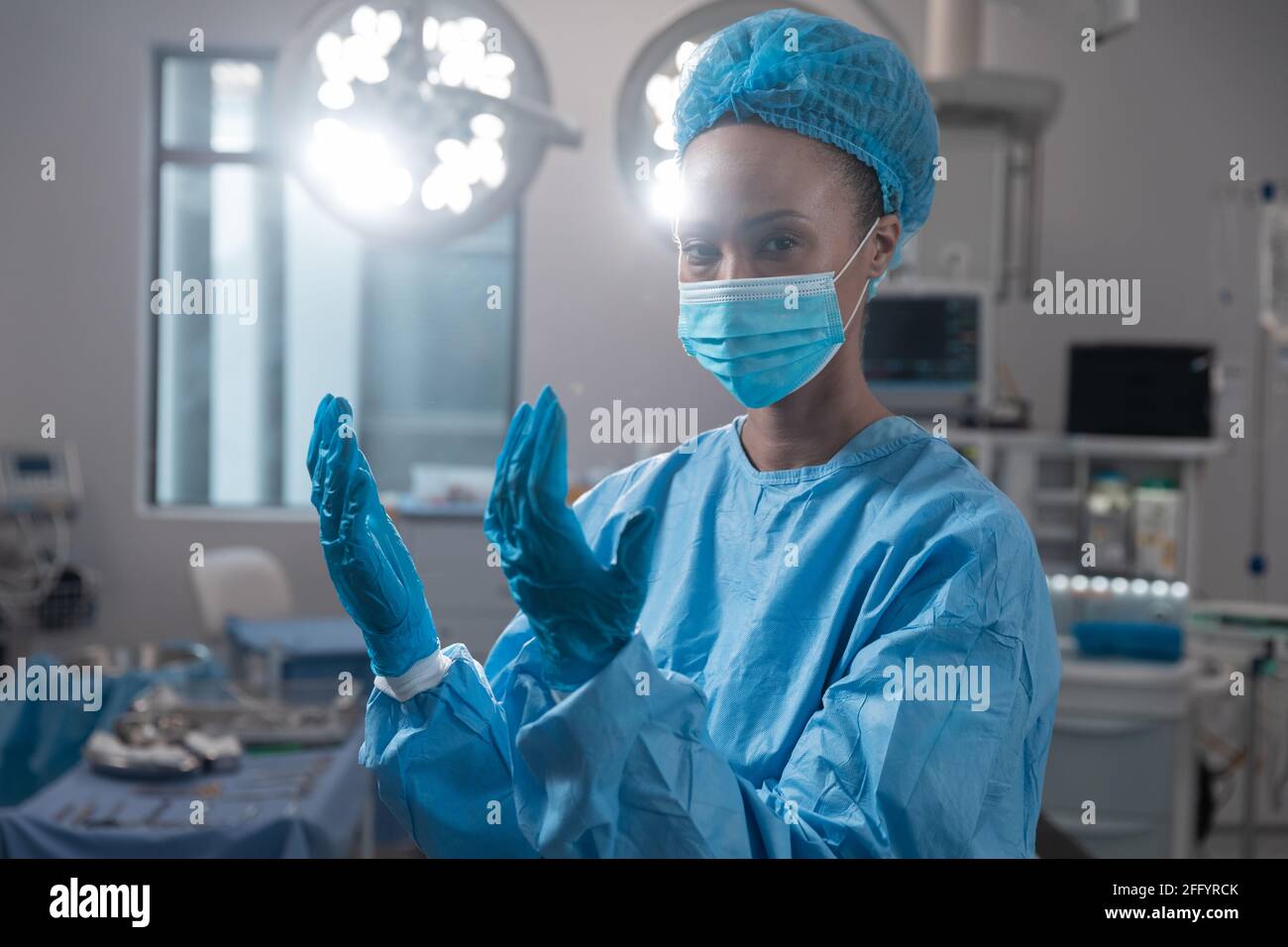 Femme chirurgien de race mixte portant un masque facial et des vêtements de protection en salle d'opération Banque D'Images