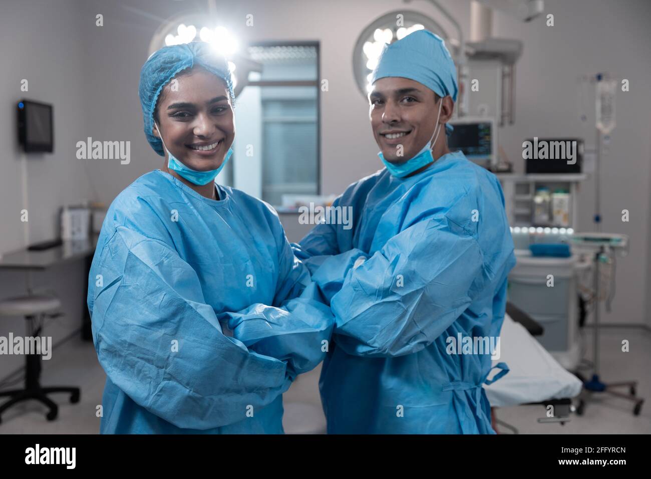 Souriant divers chirurgiens masculins féminins avec masques et protecteurs vêtements en salle d'opération Banque D'Images