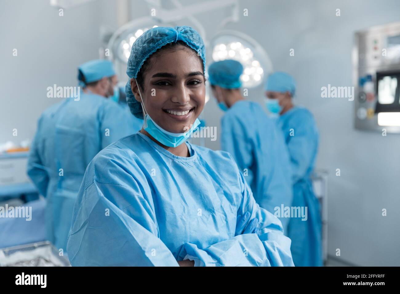 Femme souriante de race mixte chirurgien avec masque facial et protecteur vêtements en salle d'opération Banque D'Images