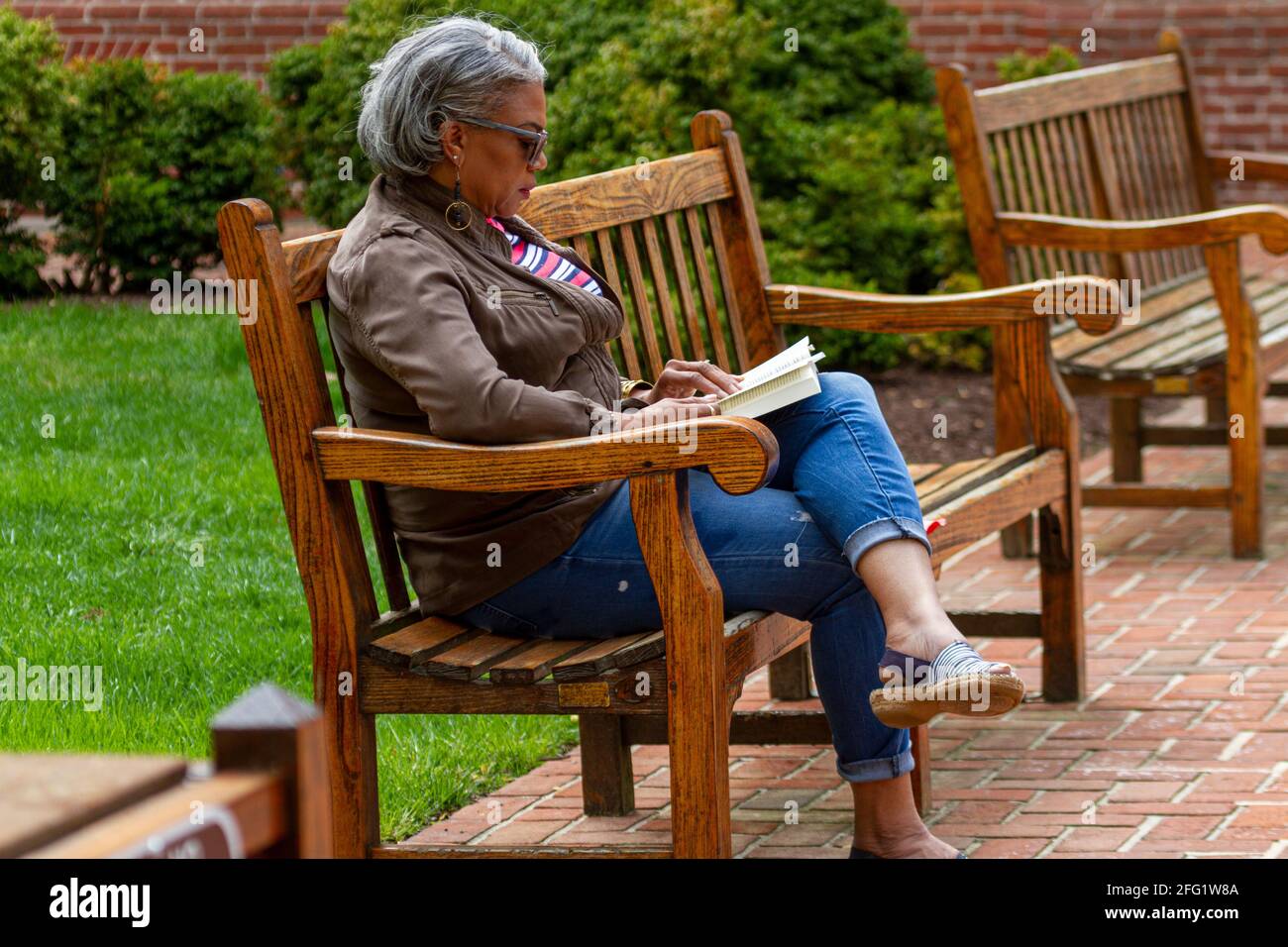 Easton, MD, USA 04-18-2021: Une femme afro-américaine âgée est assise seule sur un banc de bois au parc et lit un livre en profitant de la belle weat Banque D'Images