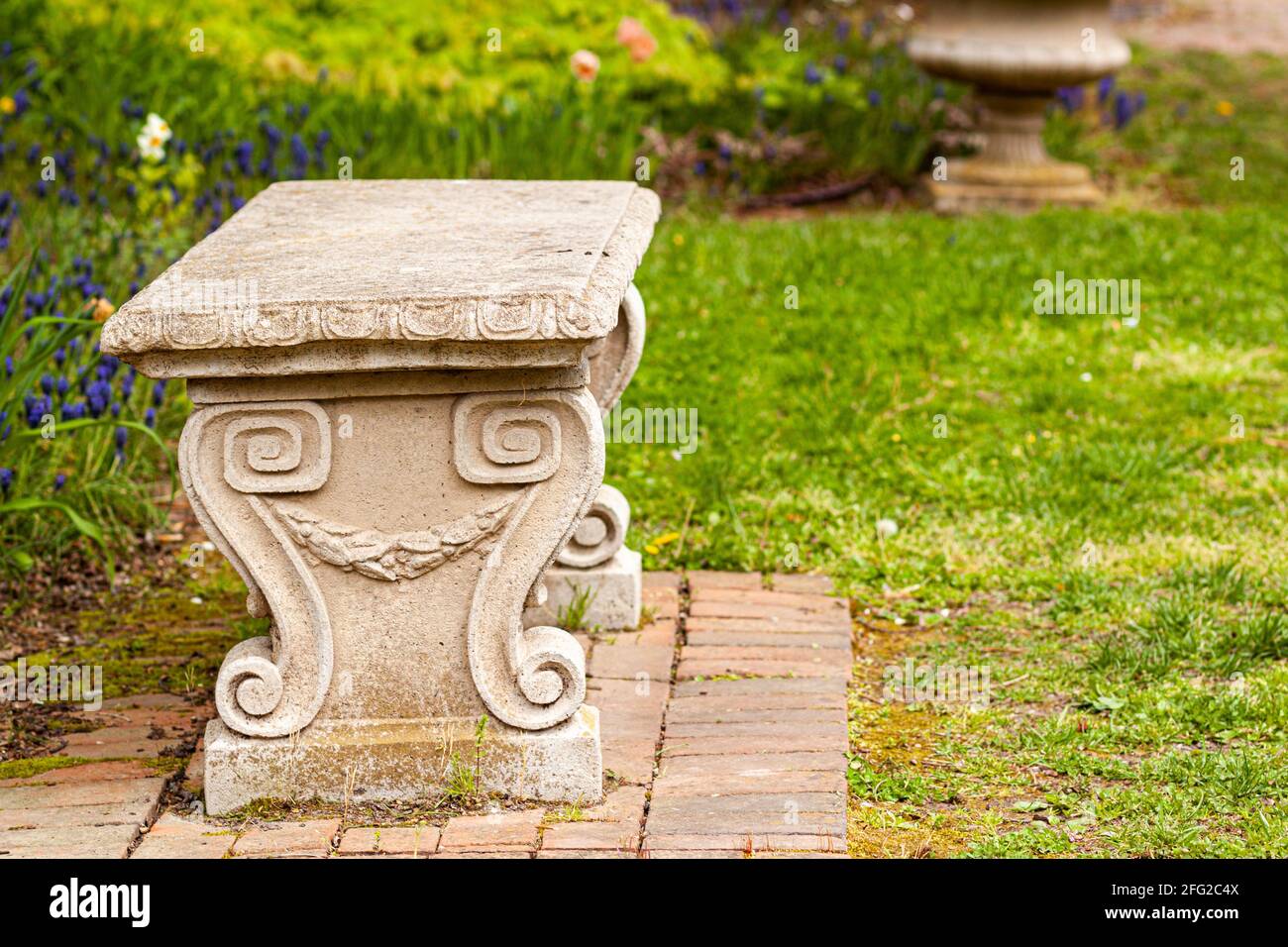 Un banc de jardin en pierre sculpté d'époque sur un terrain d'herbe dans un parc ou un jardin. Il a des motifs symétriques en spirale rappelant les figues grecques ou romaines anciennes Banque D'Images