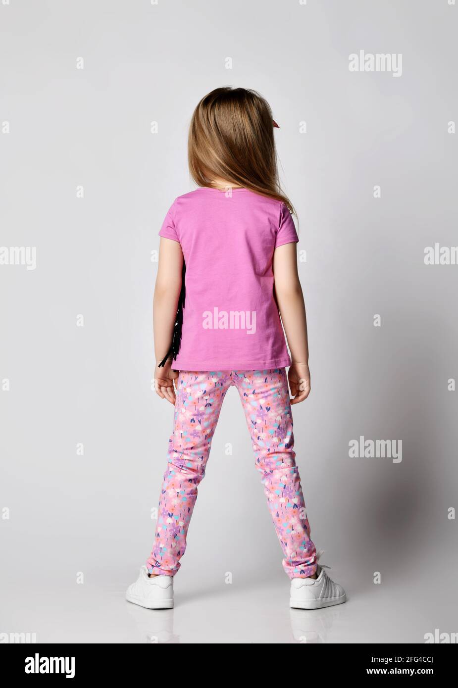 Petite fille blonde enfant en vêtements d'été pantalon coloré et le t-shirt  rose est toujours de retour à l'appareil photo Photo Stock - Alamy