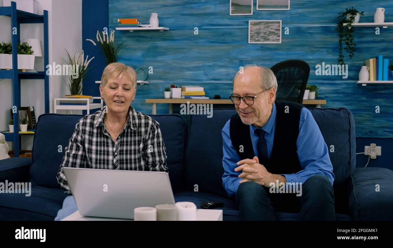 Couple d'âge plus âgé assis sur un canapé en agitant à l'appareil photo pendant la vidéo avec des neveux utilisant un ordinateur portable dans la salle de séjour. Personne senior utilisant la technologie de chat en ligne vidéo webcam réunion virtuelle conférence en ligne Banque D'Images