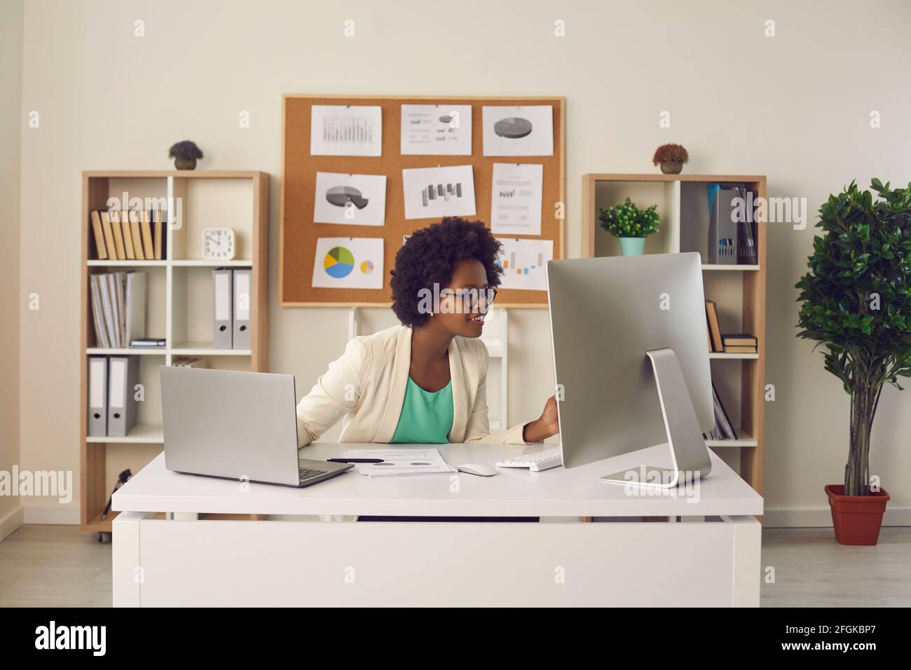 Femme secrétaire travaillant simultanément sur un ordinateur et un ordinateur portable assis sur son lieu de travail. Banque D'Images
