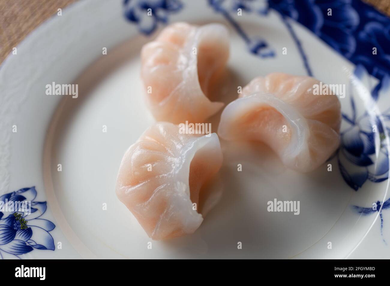 Plat traditionnel chinois authentique : boulettes de style cantonais Har gow aux crevettes, gros plan sur une assiette blanche et bleue Banque D'Images