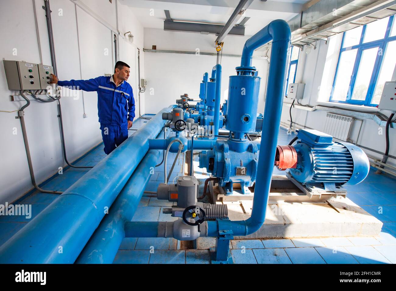 Kyzylorda, Kazakhstan: Station de purification de l'eau. Les travailleurs asiatiques contrôlent les pompes à eau. Tuyau bleu au premier plan, lumière du soleil. Sol carrelé bleu. Banque D'Images