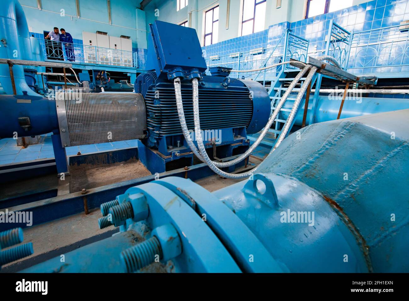 Intérieur de la station de purification d'eau. Gros plan de la pompe à moteur électrique bleue et des tuyaux. Deux hommes en arrière-plan, à gauche. Kyzylorda, Kazakhstan. Banque D'Images