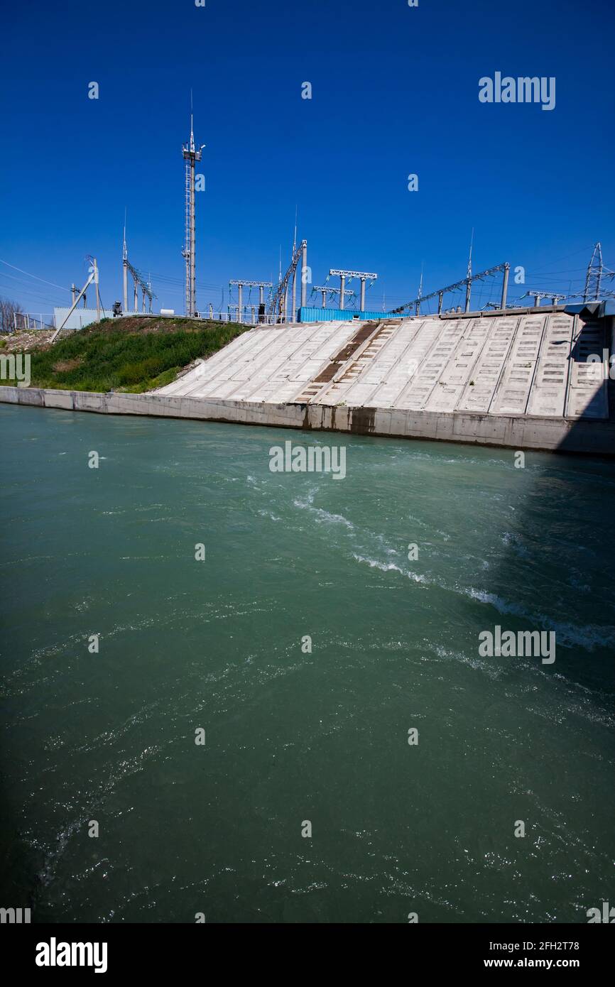 Centrale hydroélectrique. Calme de l'eau dans le canal après le barrage et la sous-station électrique à droite. Ciel bleu clair. Région d'Almaty, Kazakhstan Banque D'Images