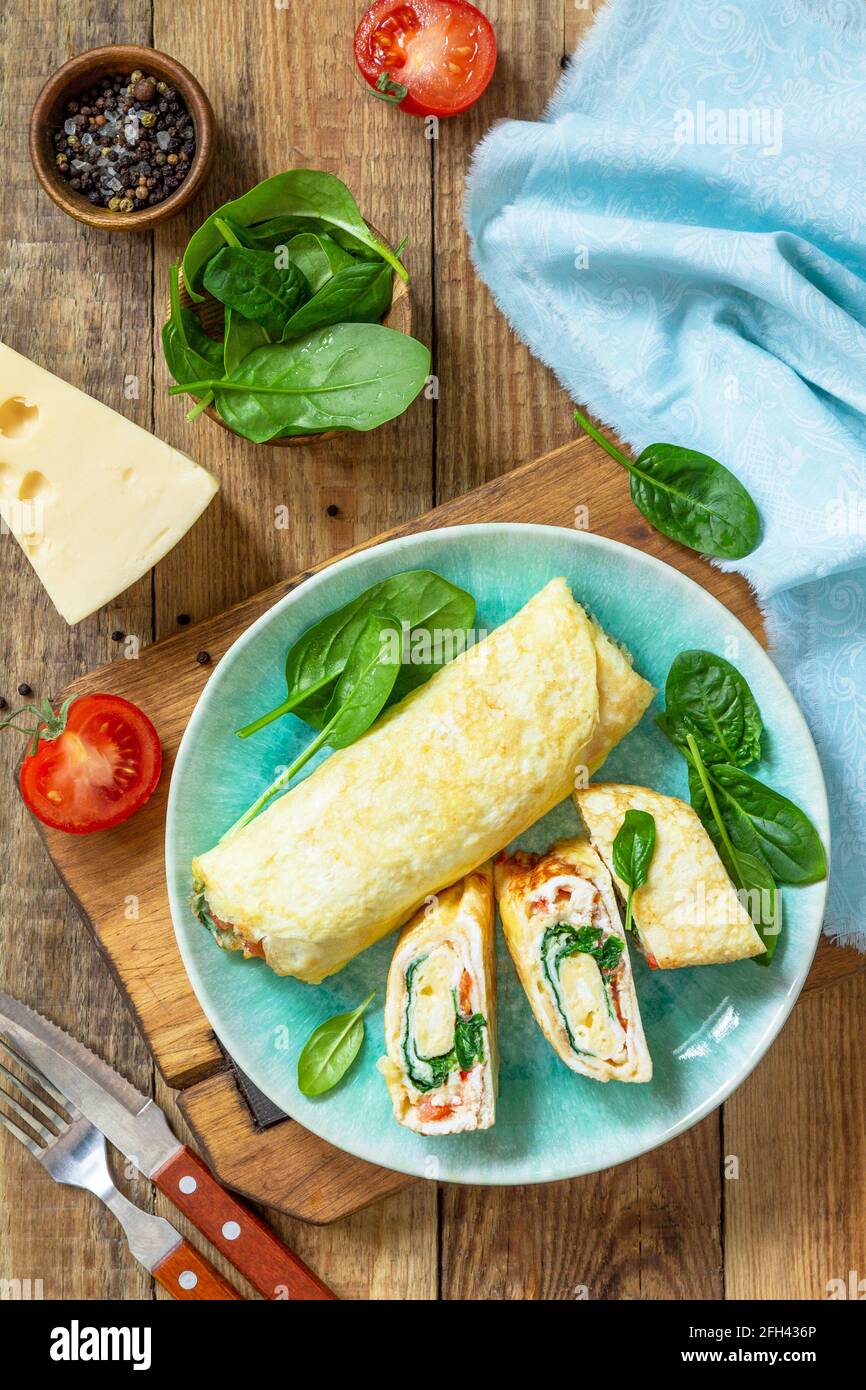 Cuisine japonaise. Plat national japonais omelette tamago yaki pour le petit-déjeuner. Œuf roulé aux épinards, à la tomate et au fromage sur une table en bois. Vue de dessus, Fla Banque D'Images