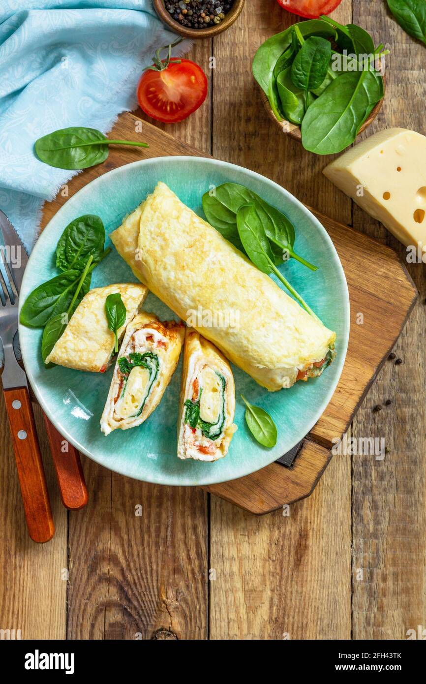 Cuisine japonaise. Plat national japonais omelette tamago yaki pour le petit-déjeuner. Œuf roulé aux épinards, à la tomate et au fromage sur une table en bois. Vue de dessus, Fla Banque D'Images