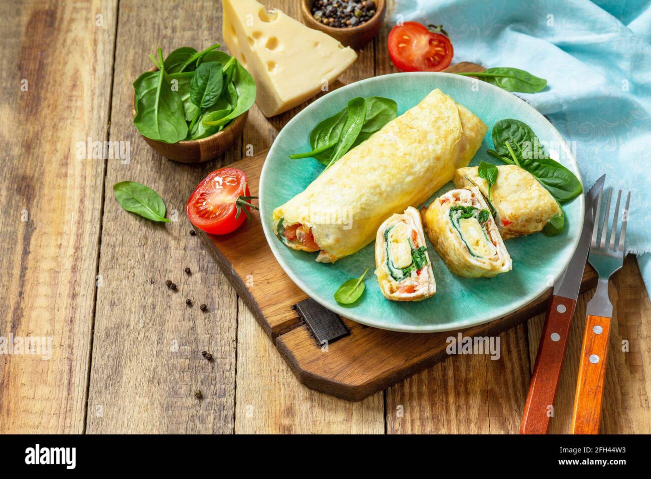 Cuisine japonaise. Plat national japonais omelette tamago yaki pour le petit-déjeuner. Œuf roulé aux épinards, à la tomate et au fromage sur une table en bois. Copier l'espace. Banque D'Images