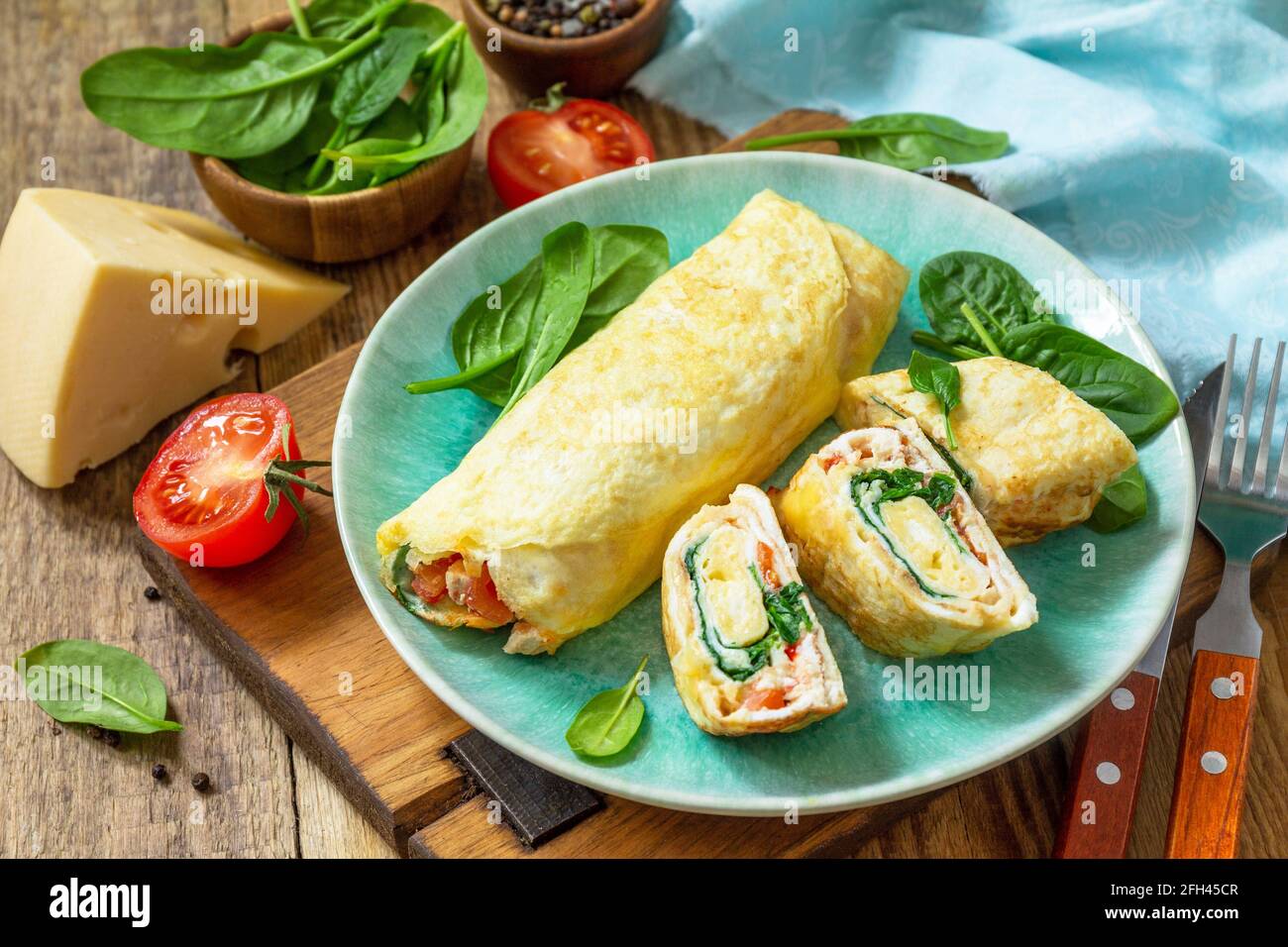 Cuisine japonaise. Plat national japonais omelette tamago yaki pour le petit-déjeuner. Œuf roulé aux épinards, à la tomate et au fromage sur une table en bois. Banque D'Images