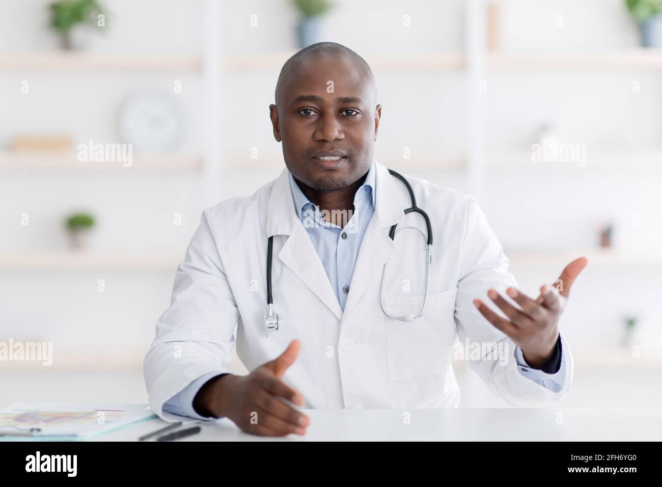 Point de vue du patient sur la consultation médicale. Un médecin de sexe masculin noir se faisant un geste pour un appareil photo dans son bureau Banque D'Images