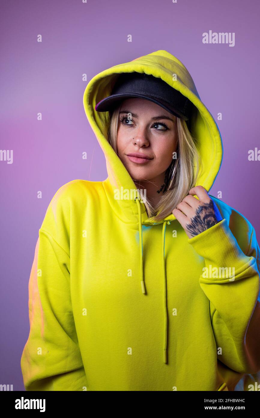 Une femme sans émotion avec un pull à capuche et une casquette de style  urbain qui ne regarde pas sur fond violet en studio avec éclairage au néon  Photo Stock - Alamy