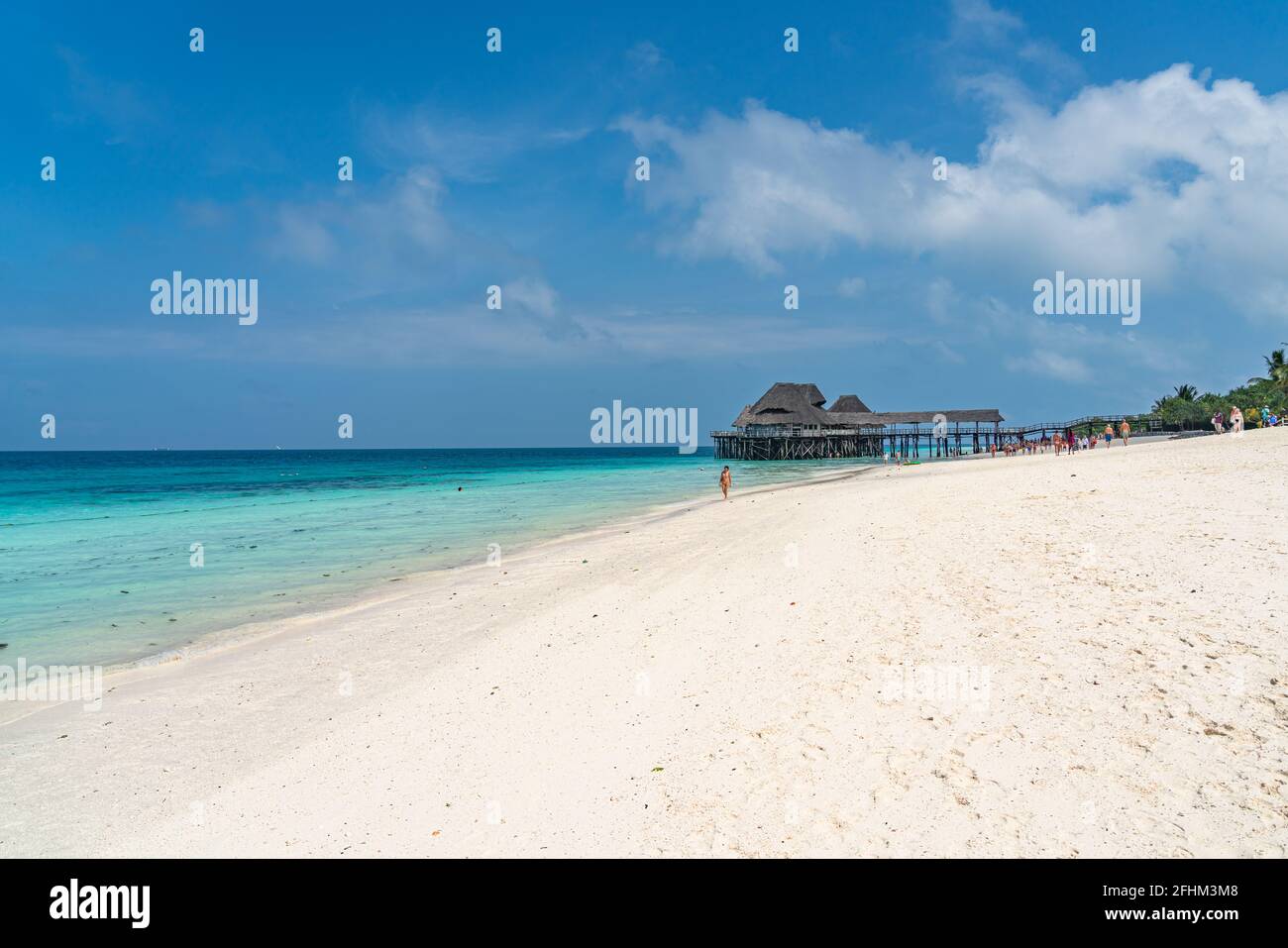 ZANZIBAR, TANZANIE - 12 FÉVRIER 2020 : personnes à la plage tropicale blanche avec un toit de chaume sur l'eau de l'île de Zanzibar. Banque D'Images