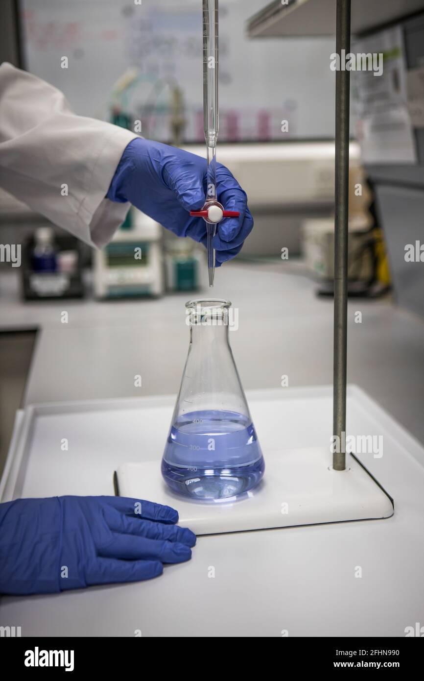 Chimiste avec mains gantées dans un laboratoire analysant un échantillon par titrage Banque D'Images