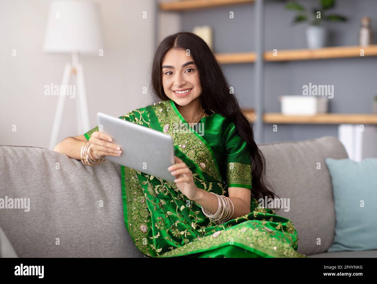 Une dame indienne joyeuse dans une cuisine traditionnelle sur un canapé confortable avec une tablette pc pour assister à une réunion en ligne depuis la maison Banque D'Images