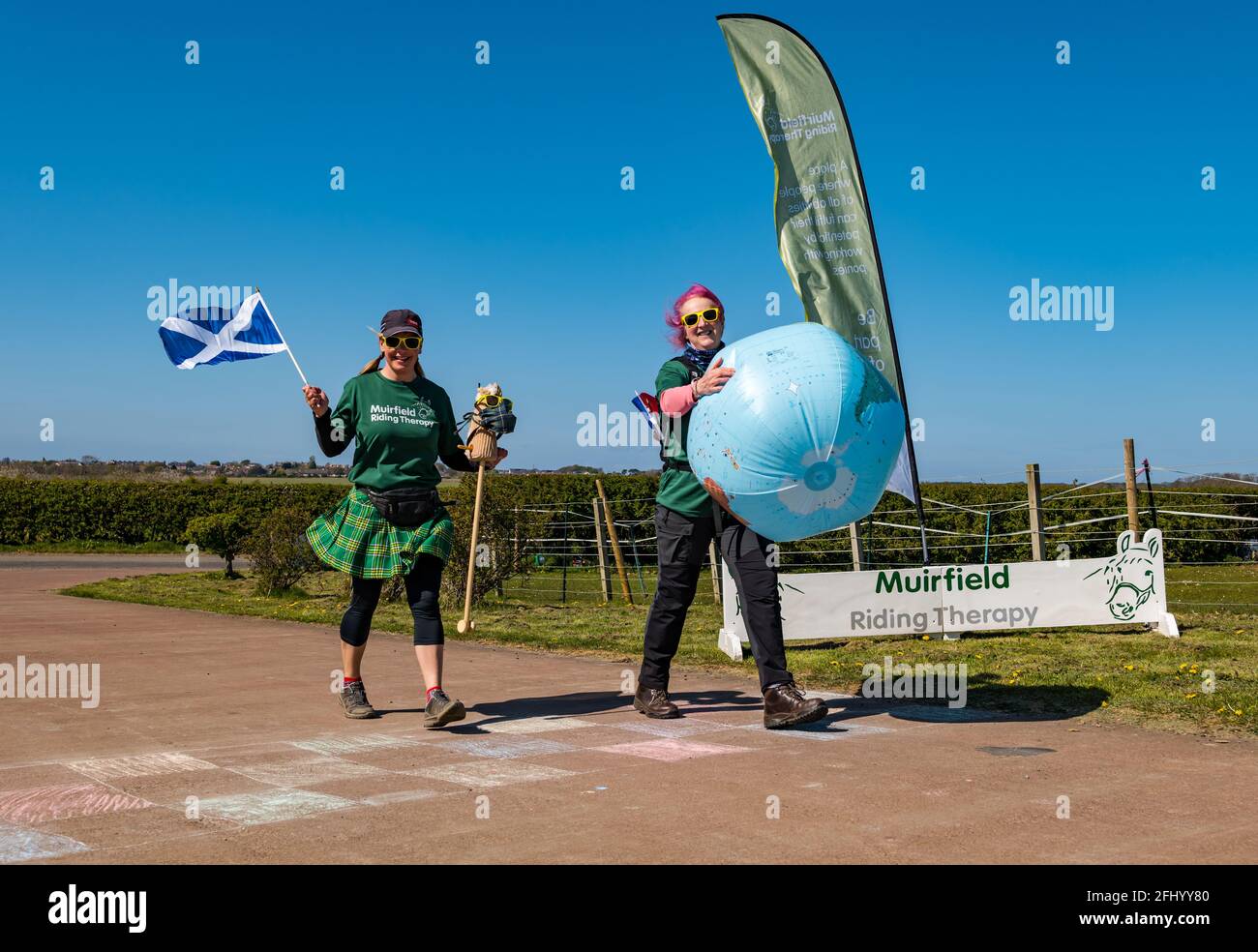 East Lothian, Écosse, Royaume-Uni, 25 avril 2021. Virtual Kilt Walk : les marcheurs de kilt soutenant la charité Muirfield Riding Therapy franchissent une ligne d'arrivée pour célébrer leur participation à leur campagne de collecte de fonds « Round the World ». Chaque équipe a choisi une destination et a parcouru, parcouru ou roulé les miles de chez elle jusqu’au point de leur choix, totalisant 24,900 miles de la circonférence de la terre et élevant plus de 10,000 £. Photo : Shirley Duff, directrice du centre et Susan Law, coordonnatrice des services Banque D'Images