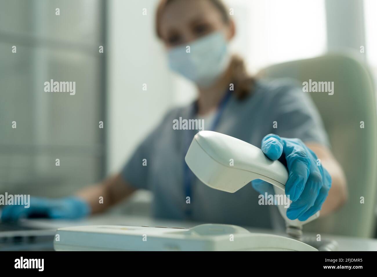 Gros plan d'un employé de laboratoire portant des gants bleus pour décrocher le téléphone lorsque vous répondez à un appel au bureau Banque D'Images