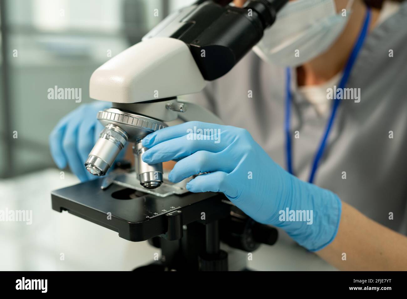 Gros plan d'un employé de laboratoire méconnaissable avec des gants bleus pour ajuster le microscope glissez en laboratoire pendant que vous faites de la recherche Banque D'Images