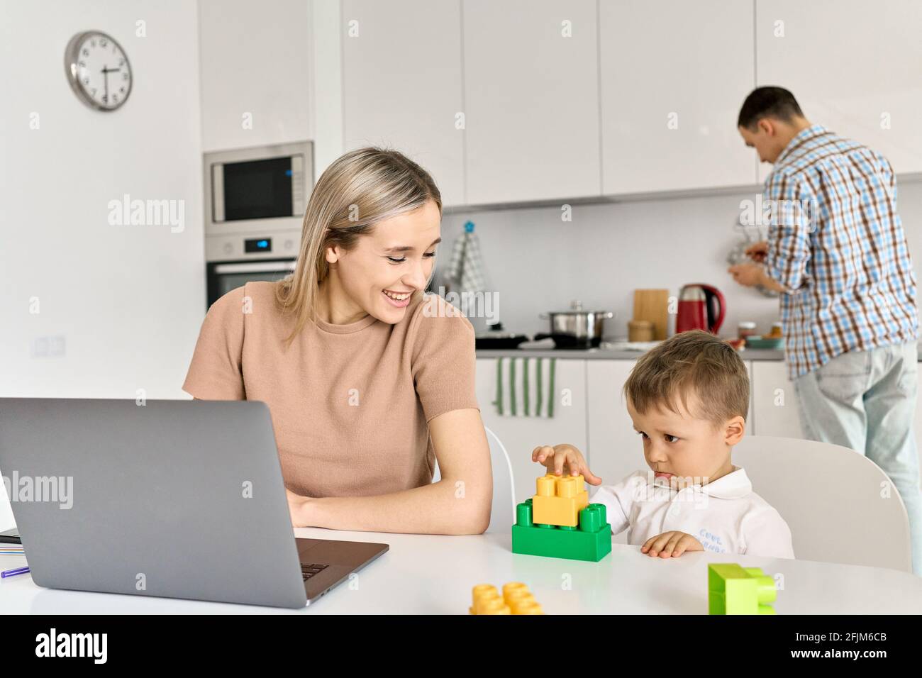 Une mère heureuse travaillant à la maison en utilisant un ordinateur portable assis à une table avec un enfant mignon fils. Banque D'Images