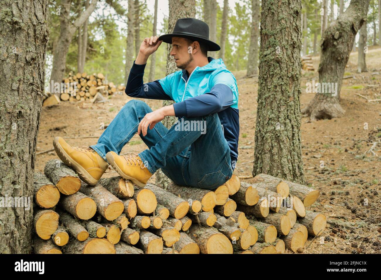 Portrait jeune homme caucasien en chapeau de cowboy noir assis sur une pile  de bois en bois dans le paysage forestier.Homme appréciant et se reposant  dans la nature Photo Stock - Alamy