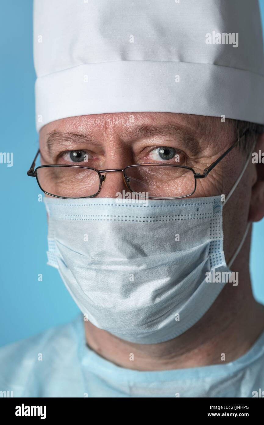 Portrait d'un médecin expérimenté d'âge moyen dans un capuchon et un masque médicaux, portant des lunettes. Vue rapprochée de la caméra Banque D'Images