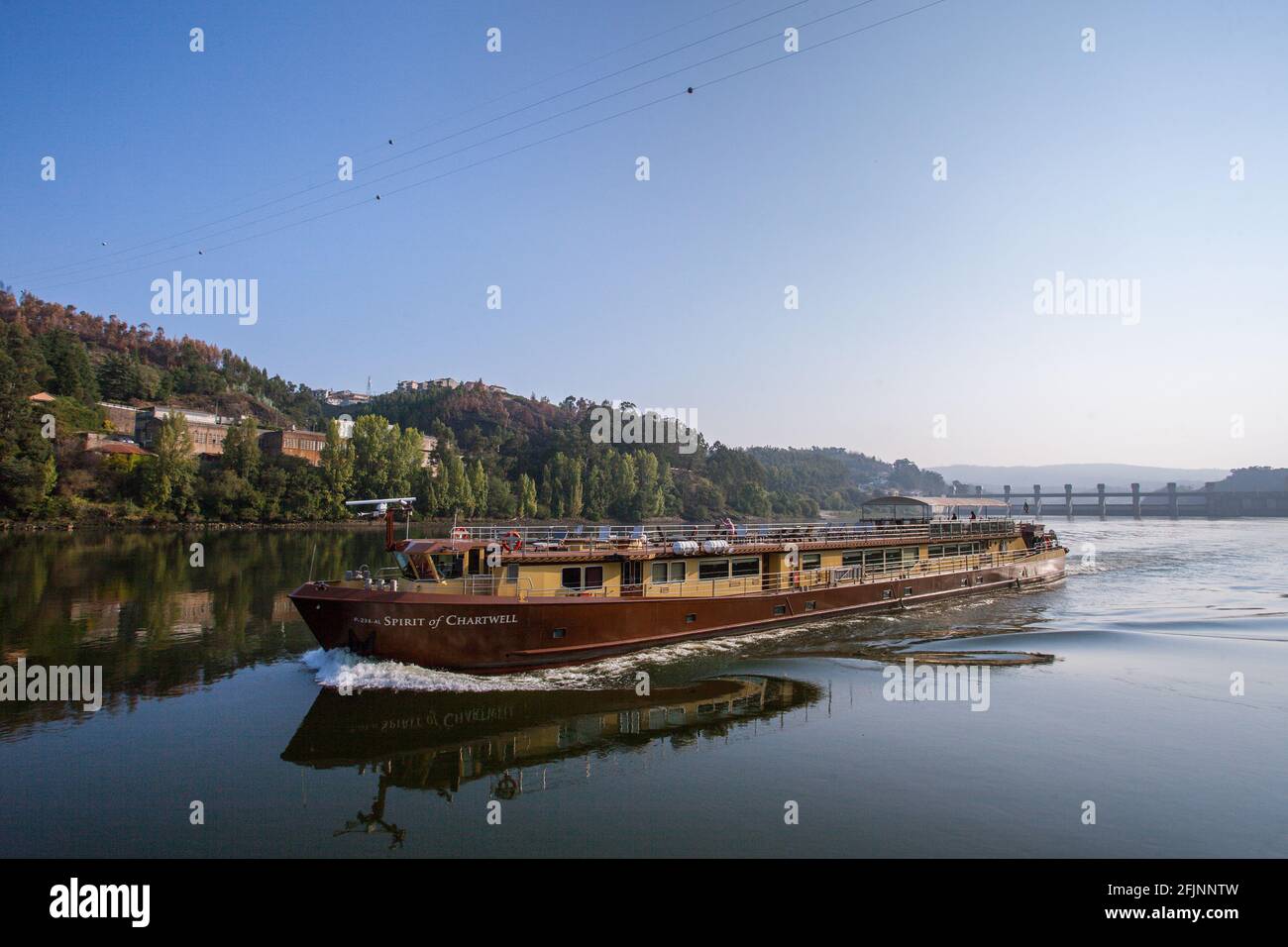 Un bateau naviguant dans la vallée du Douro, dans le nord du Portugal, avec le barrage de Crestuma-lever en arrière-plan. Banque D'Images
