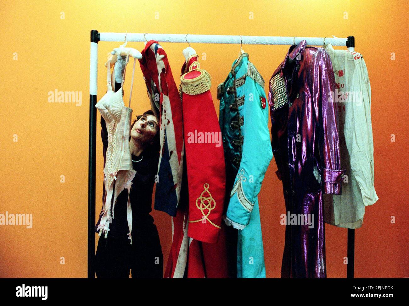 EXPOSITION DE COSTUMES DE ROLLER ET DE ROLLER AU BARBICAN.LISA COLLINS DU BARBICAN AVEC, SUR LE RACK L-R: MADONNA JEAN-PAUL GAULTIER BUSTIER; DAVID BOWIE'S UNION JACK FROCK COAT; GEORGE HARRISONS RED COAT DE SGT. PEPPER; COAT BLEU DE PAUL MCCARTNEY DE SGT. POIVRE ET ROBE VIOLETTE DU PRINCE. Banque D'Images