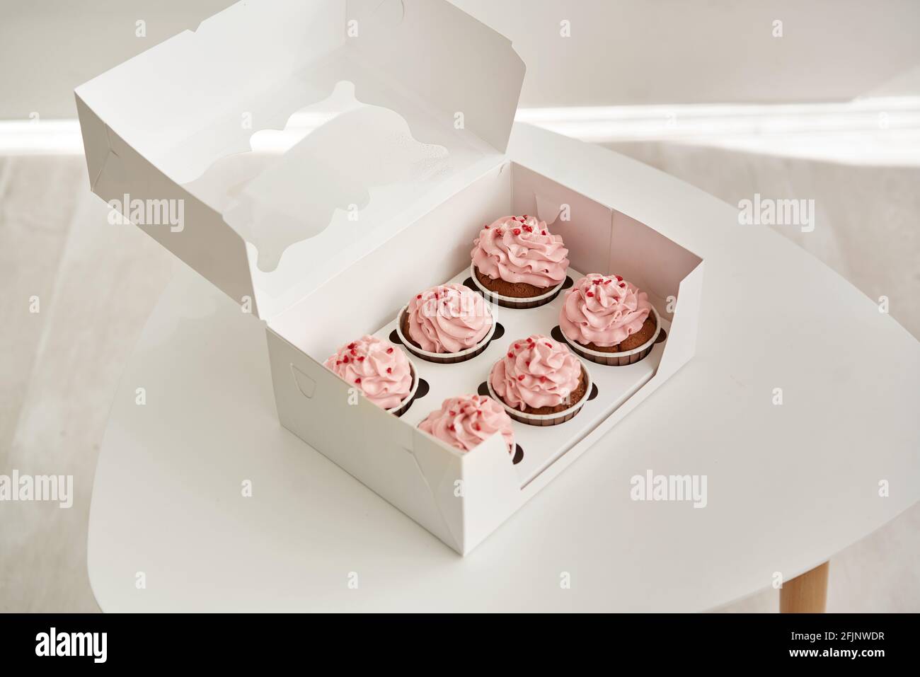 Petits gâteaux roses dans la boîte cadeau sur la table blanche. Banque D'Images