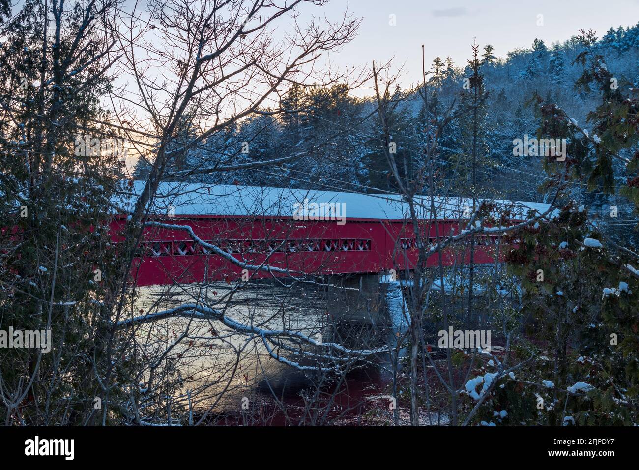 Pont couvert rouge en hiver avec arbres et rivière en arrière-plan Banque D'Images