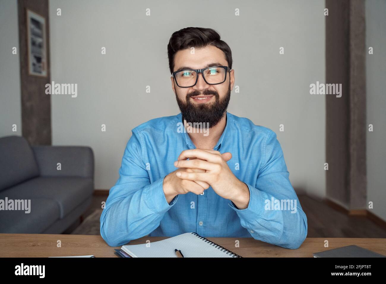 Homme intelligent indépendant en lunettes regardant la caméra pendant qu'il est assis au bureau Banque D'Images