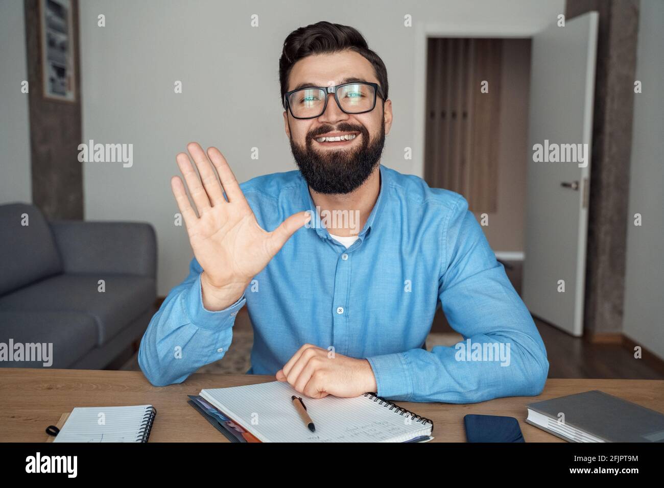 Homme caucasien millénaire souriant au bureau regardant la caméra main onduleuse Banque D'Images