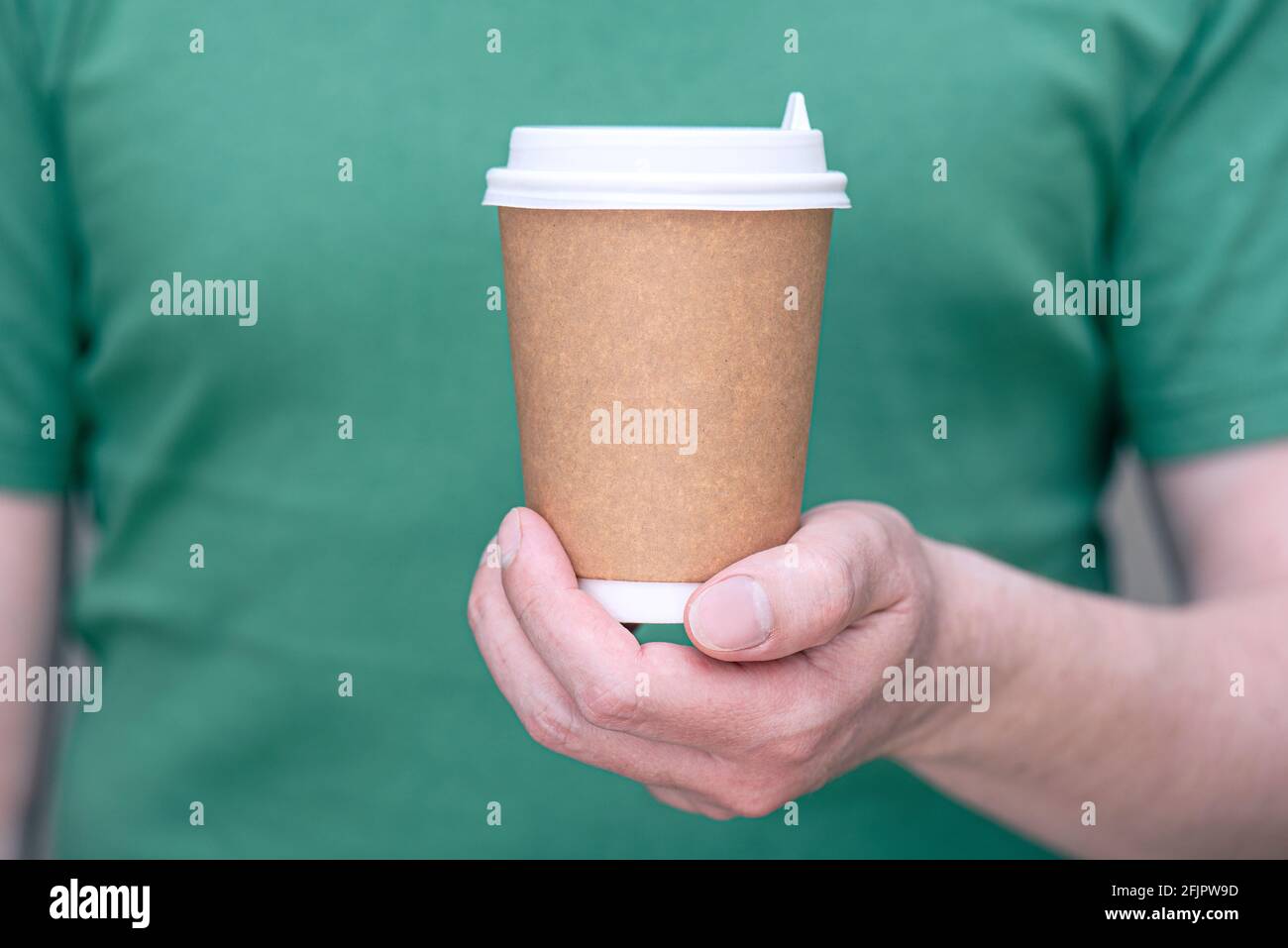 Un homme en t-shirt vert tenant une tasse de papier brun avec boisson - café ou thé, mug pour emporter, maquette avec espace pour le texte Banque D'Images