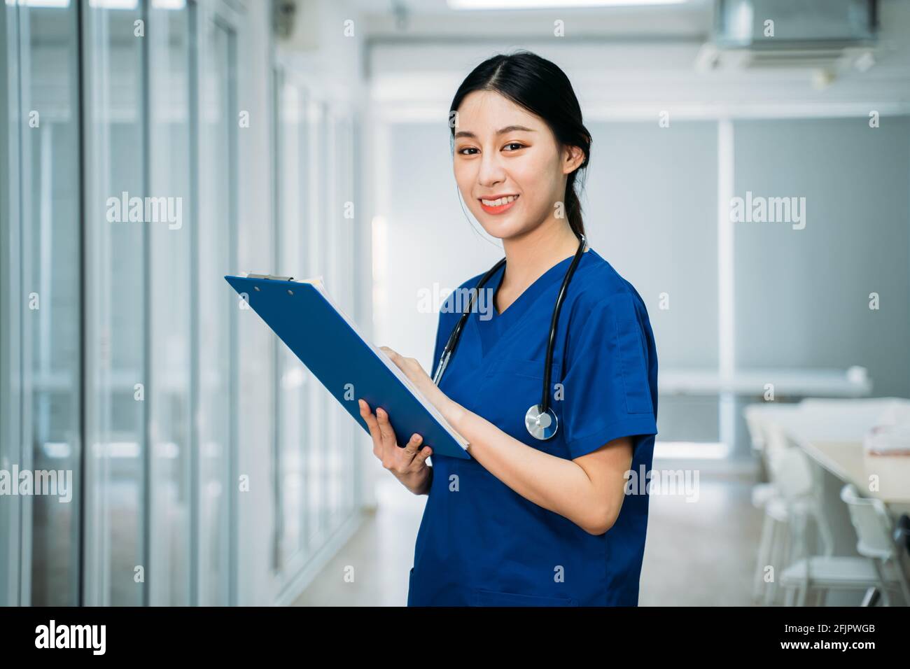Portrait de jeune femme asiatique en uniforme bleu avec un stéthoscope placé dans le couloir de l'hôpital et contenant les rapports de vérification du presse-papiers lorsque vous regardez l'appareil photo Banque D'Images