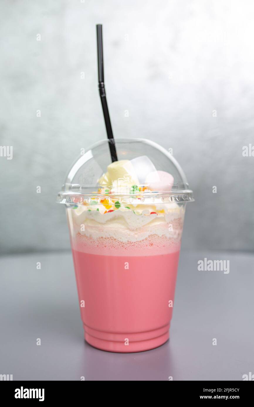 cocktail rose laiteux-rose dans une tasse en plastique avec une paille. Banque D'Images
