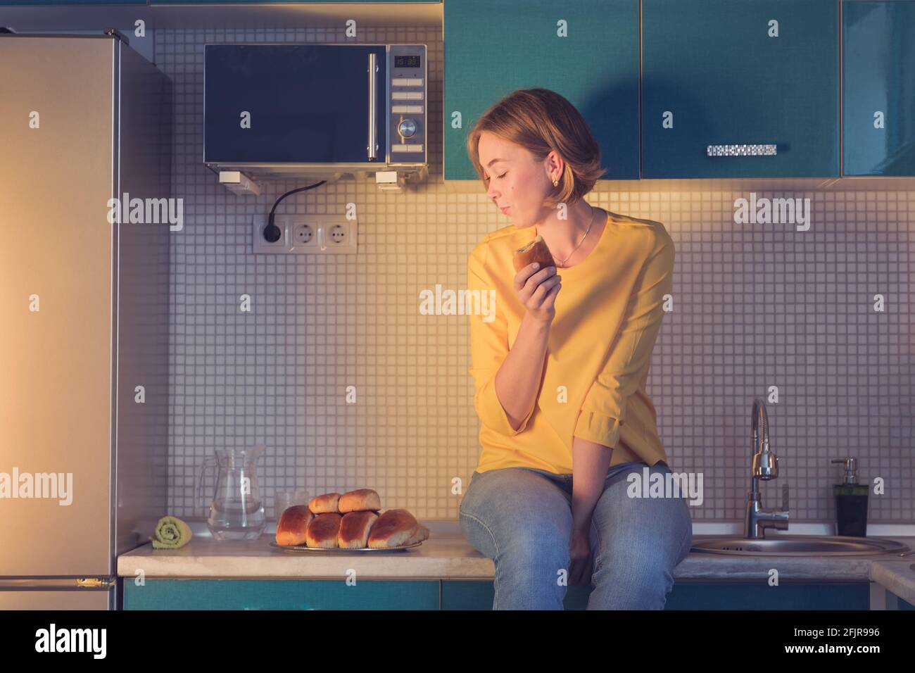 portrait d'une fille qui regarde avec plaisir les pâtisseries assis sur la table dans la cuisine. Banque D'Images