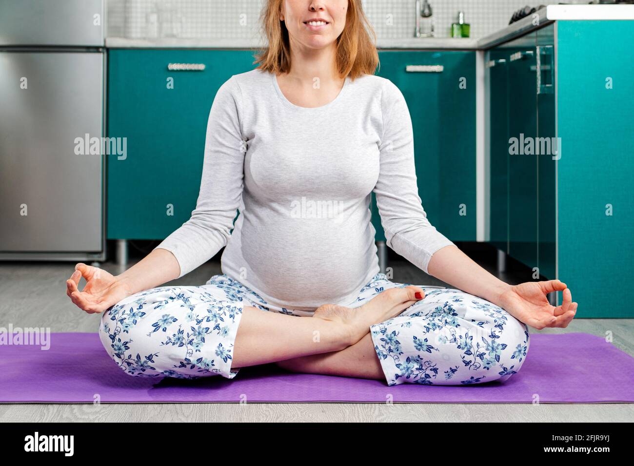 Une femme caucasienne enceinte fait du yoga et médite sur un tapis. La cuisine est en arrière-plan. Concept de santé et de yoga pour la grossesse WO Banque D'Images