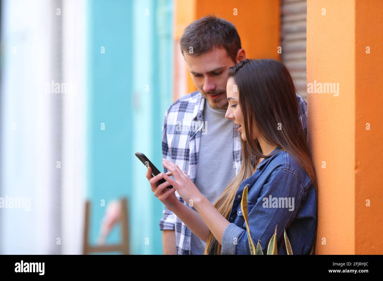 Deux amis qui utilisent un smartphone parlent de contenu en ligne dans une rue colorée Banque D'Images