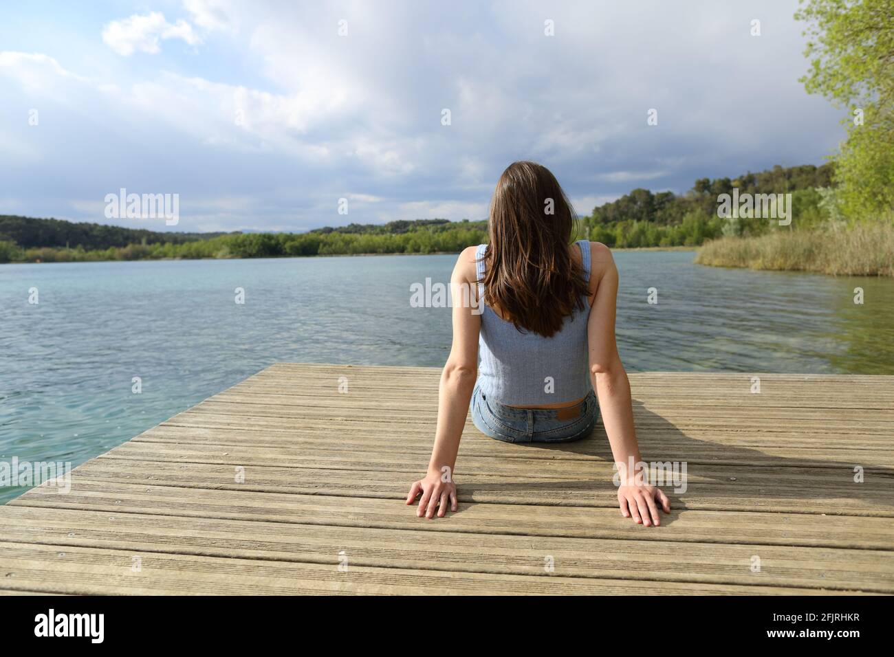 Vue arrière portrait d'une femme assise relaxante dans un lake pier en vacances d'été Banque D'Images