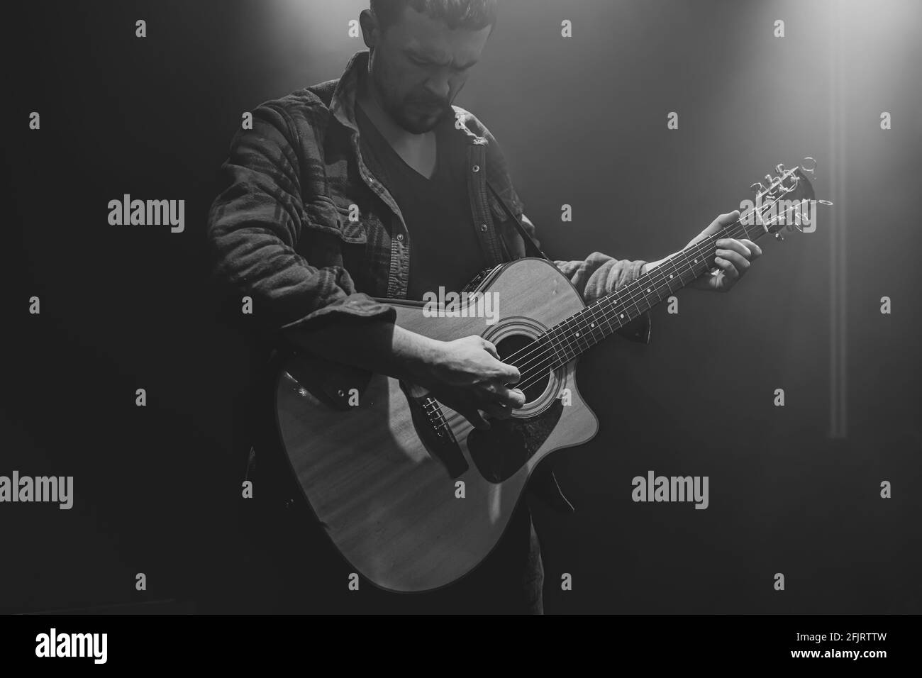 Un homme joue une guitare acoustique à un concert partiellement éclairé. Banque D'Images