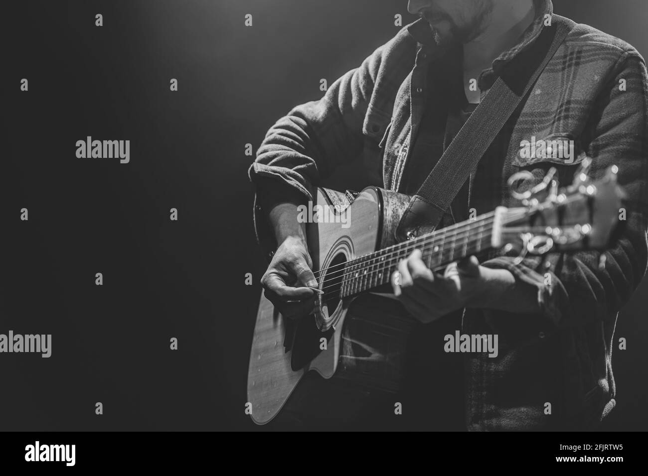 Musicien de sexe masculin jouant de la guitare acoustique dans un espace de copie de pièce sombre. Banque D'Images