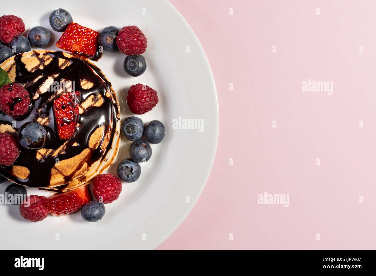 vue de dessus d'un dessert de crêpes aux fruits et au chocolat sur une assiette blanche sur fond rose Banque D'Images